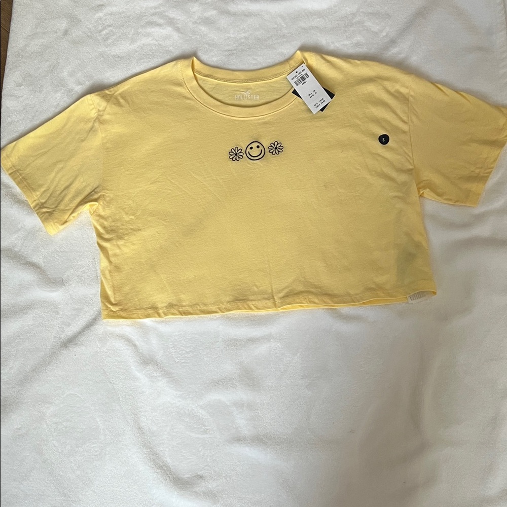 Hollister Yellow Crop Tee with Smiley and Flower Design.